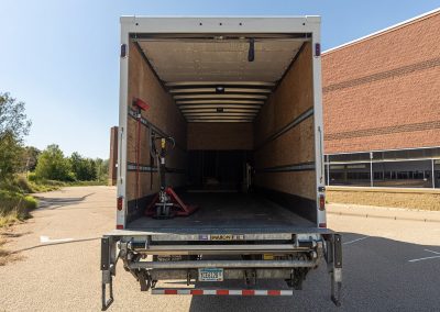 Open rear of an Elite Transportation Systems dock truck showing the empty deck, pallet jack, and liftgate