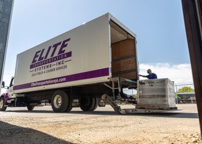 Elite Transportation Systems driver guiding a shrink-wrapped pallet onto the liftgate of a dock truck