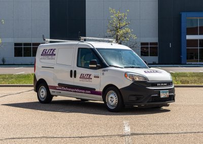 Elite Transportation Systems small cargo van with roof rack parked outside a commercial office building