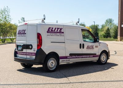 Rear three-quarter view of an Elite Transportation Systems small cargo van with a roof rack in a parking lot