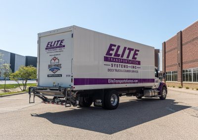 Rear three-quarter view of an Elite Transportation Systems 26-foot dock truck with the liftgate folded up