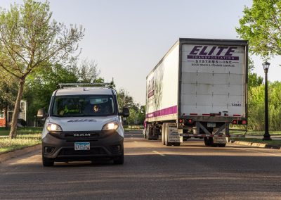 Elite Transportation Systems small cargo van and a semi dry van sharing a residential street at golden hour