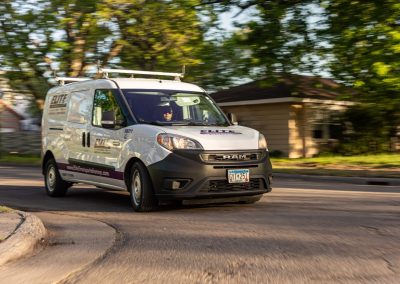 Elite Transportation Systems small cargo van driving a tree-lined residential street, contract driver at the wheel