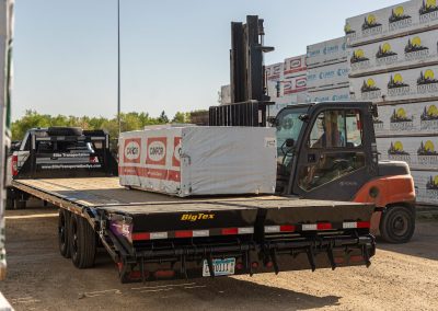 Forklift loading a wrapped lumber bundle onto an Elite Transportation Systems gooseneck flatbed