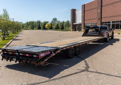 Rear view of an Elite Transportation Systems gooseneck flatbed trailer with wood deck and fold-down ramps