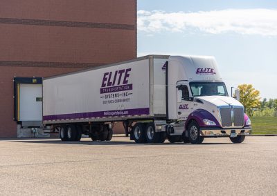 Elite Transportation Systems 53-foot dry van backed into a loading dock at a brick warehouse, driver in the cab