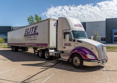 Elite Transportation Systems semi and 53-foot dry van parked outside a distribution warehouse under a blue sky