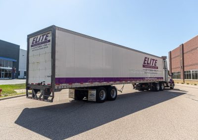 Rear three-quarter view of an Elite Transportation Systems 53-foot dry van trailer parked between warehouse buildings