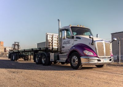 Elite Transportation Systems semi flatbed with forklift stowed at the rear, parked on gravel in evening light