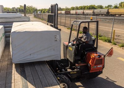 Elite Transportation Systems operator sets a wrapped bundle of lumber onto the flatbed deck beside a rail yard
