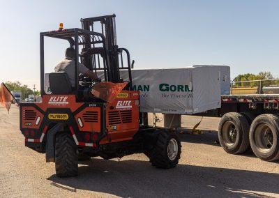 Elite Transportation Systems operator drives a Palfinger forklift carrying a wrapped bundle of lumber toward the flatbed