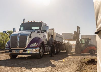 Elite Transportation Systems driver at the flatbed while a piggyback forklift unloads wrapped building materials at a jobsite